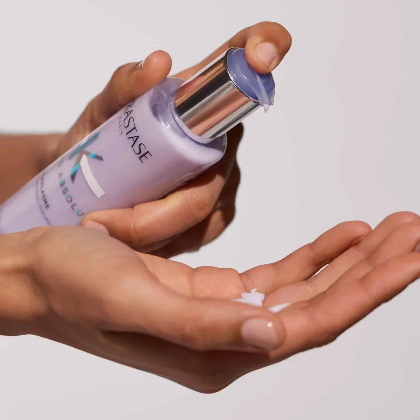 one hand holding and squeezing Kerastase cicaflash serum onto other hand