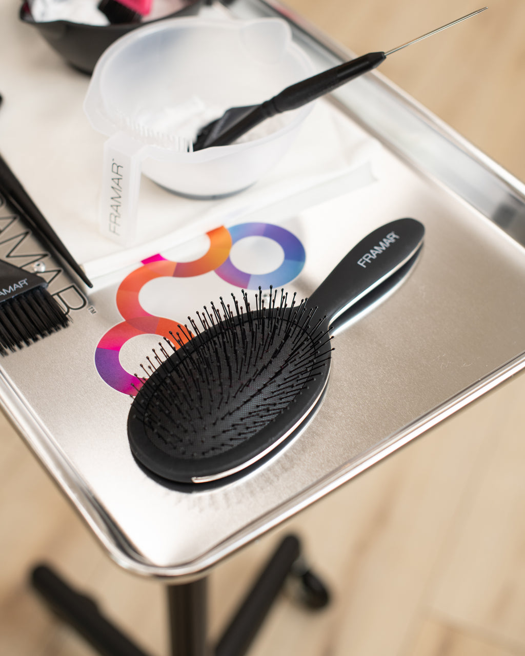 Black hairbrush on a metal tray with a colorful logo in the background
