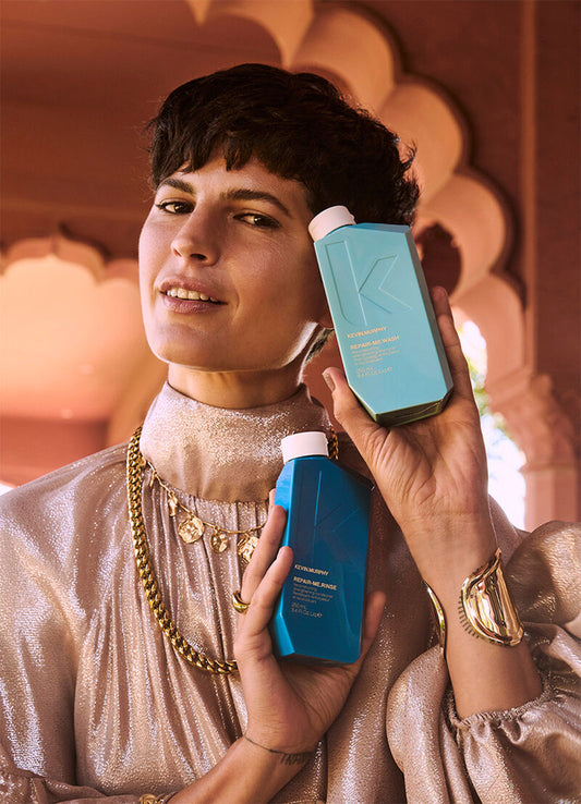 Woman with brunette short hair holding in her hands a blight blue bottle and a dark blue bottle of shampoos