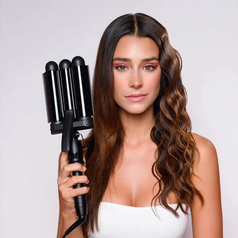 Woman with styled hair holding a hair styling tool against a plain background