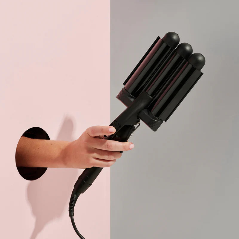 Hand holding a black hair styling tool against a pink and gray background