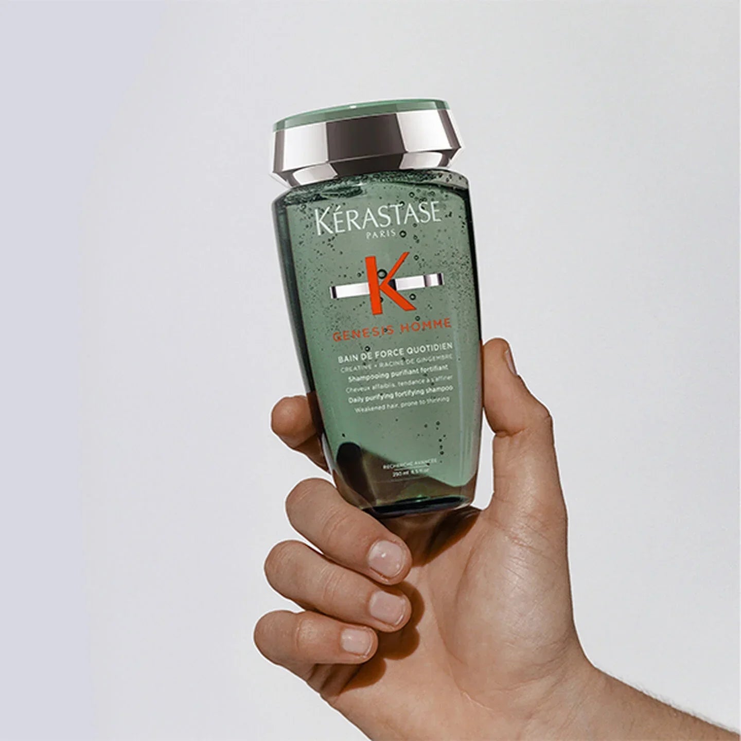 Hand holding a bottle of Kérastase shampoo against a light background
