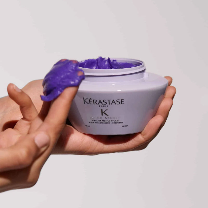 Kérastase hair mask with purple cream being scooped out by a hand on a light gray background