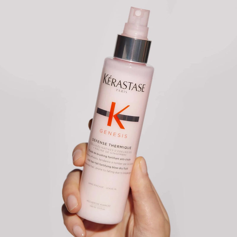 Kérastase bottle held in a hand against a plain background