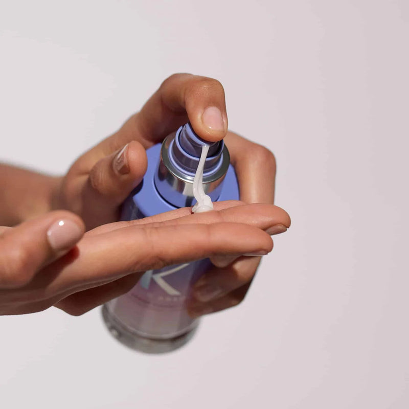 Hand applying a small amount of cream from a blue container onto the palm against a light background