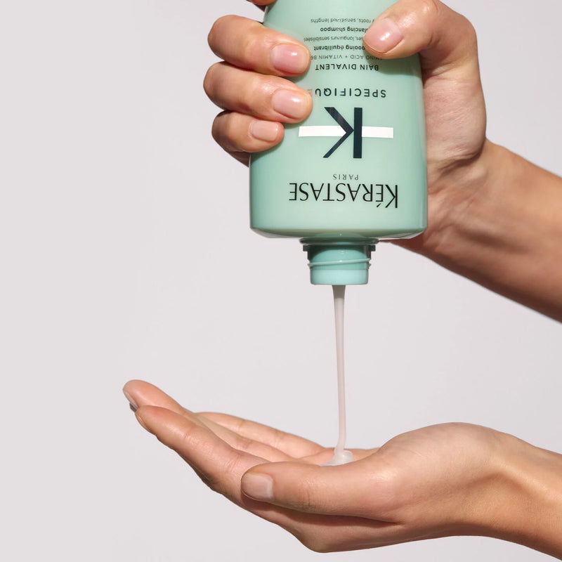 Person holding a Kérastase bottle with product being dispensed onto a palm against a neutral background