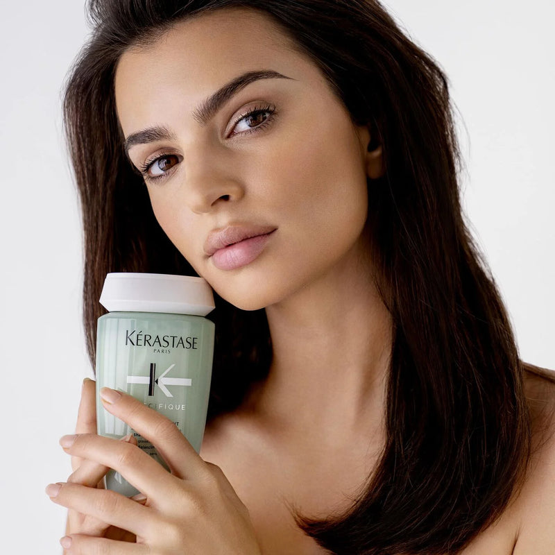 Woman holding a Kérastase product against a plain background