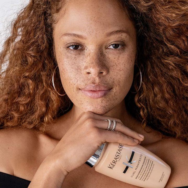 Woman holding a Kerastase bottle with a neutral background