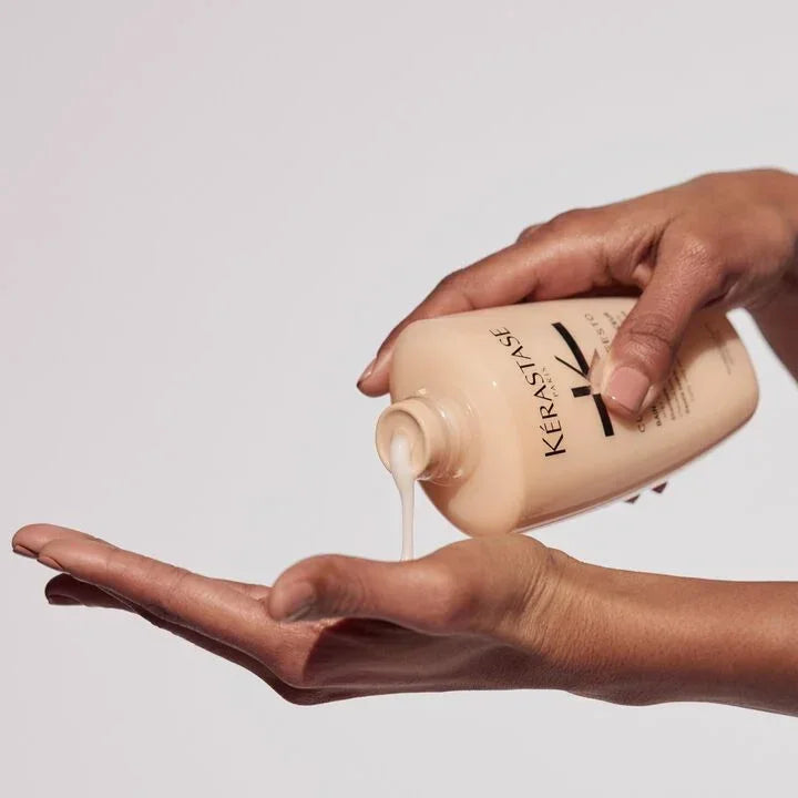 Hand pouring Kérastase product into another hand against a neutral background