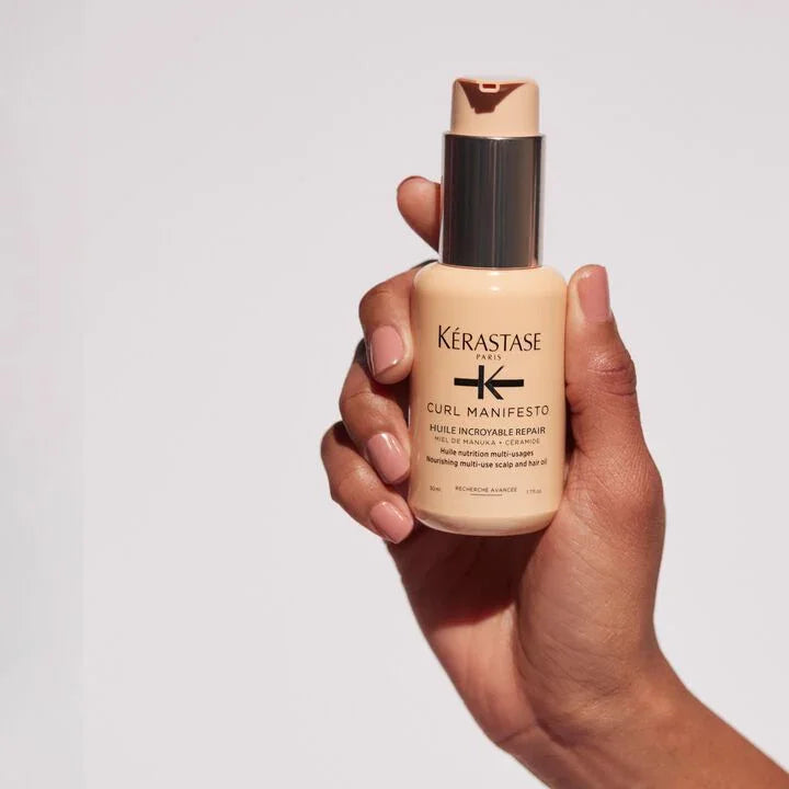 Hand holding a bottle of Kerastase Curl Manifesto product against a light gray background