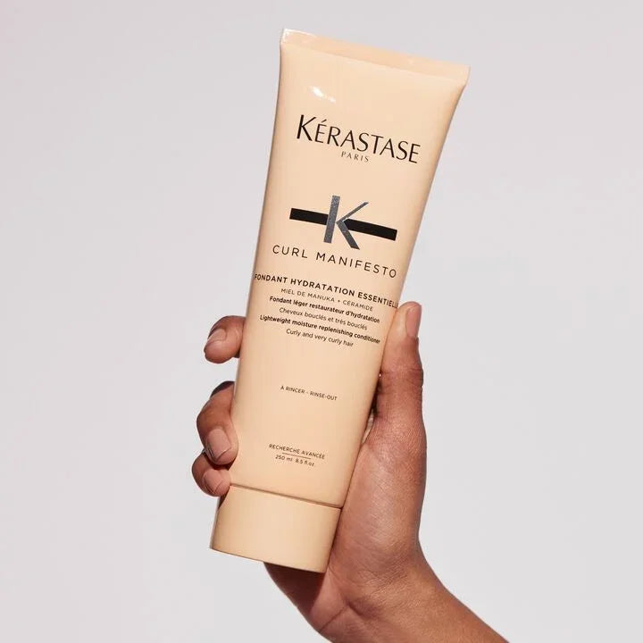 Hand holding a Kérastase Curl Manifesto product against a light gray background
