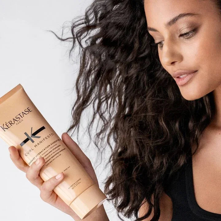 Woman holding a Kérastase hair care product with styled hair against a white background