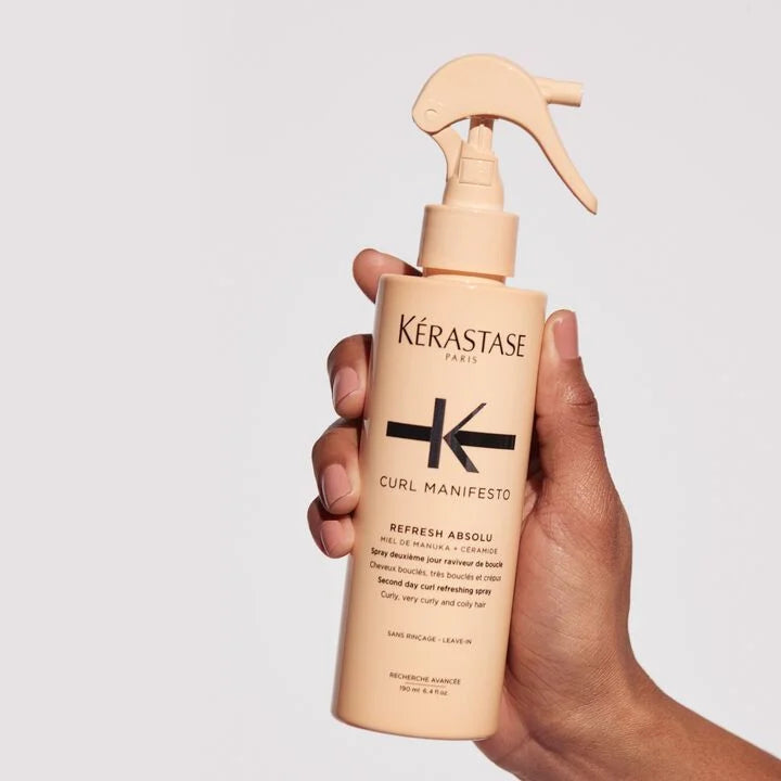 Kérastase Curl Manifesto spray bottle held in a hand against a light gray background