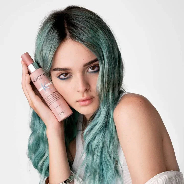 Woman with teal hair holding a pink bottle against a white background