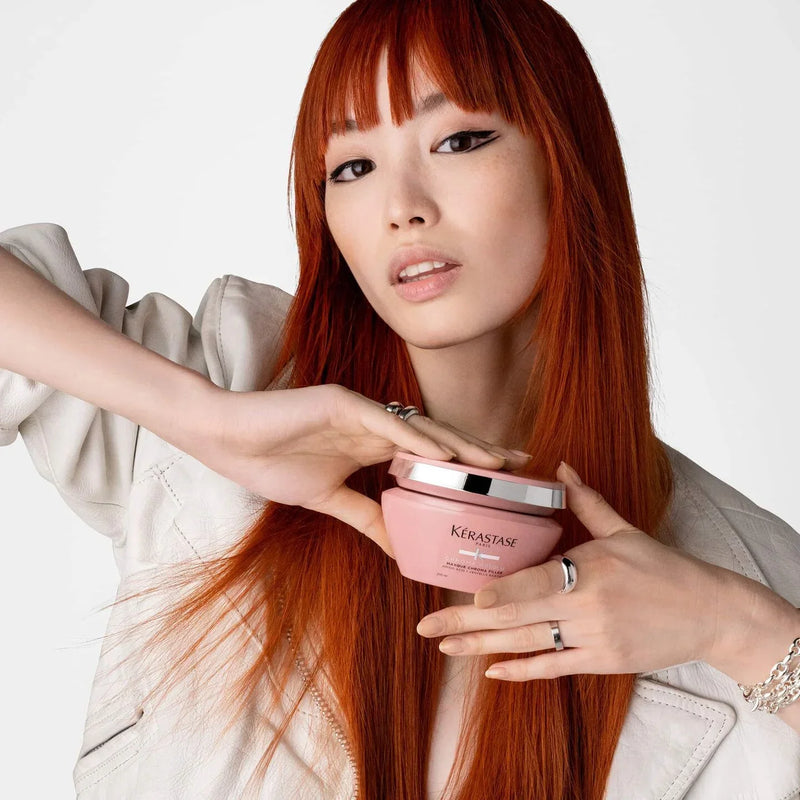 Woman with red hair holding a pink Kerastase product against a white background
