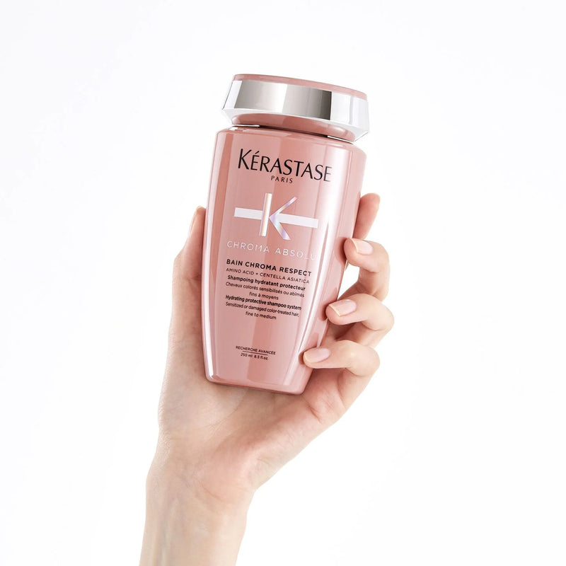 Hand holding a Kérastase shampoo bottle on a white background