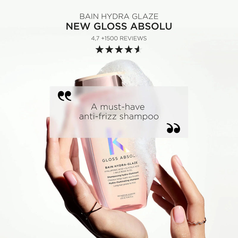 Hand holding a bottle of Kérastase Gloss Absolu shampoo with product packaging in the background.