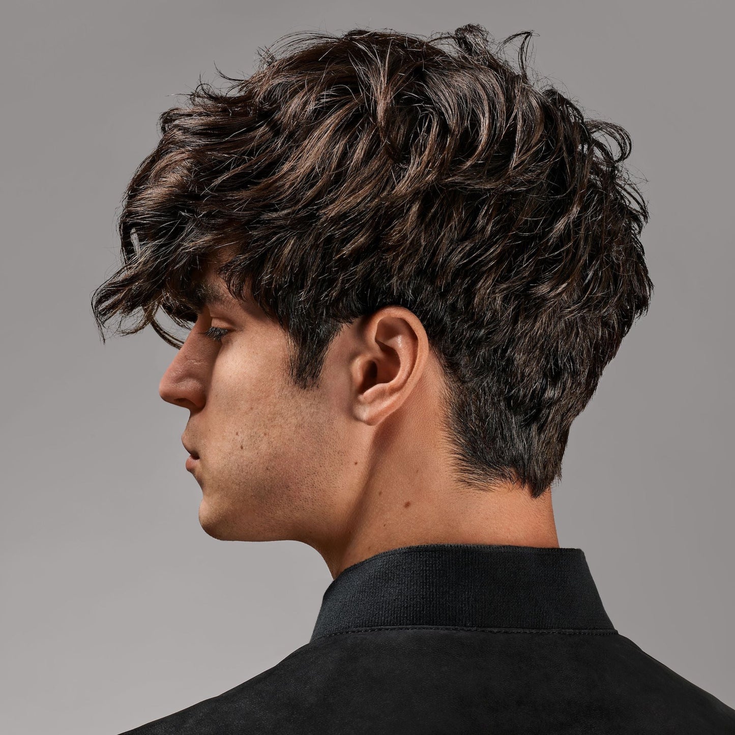 Side profile of a person with styled dark hair against a gray background