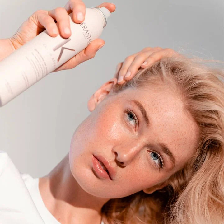 Woman applying hair product to her hair with a focus on the product bottle.