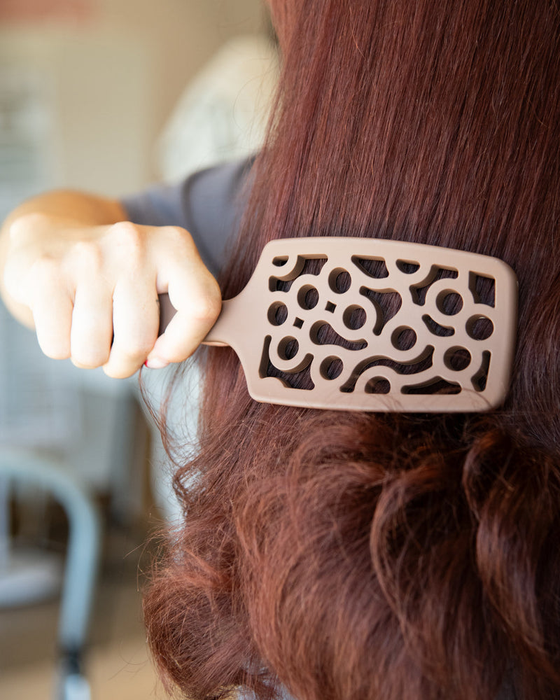 Person using a decorative hairbrush on their hair with a blurred background