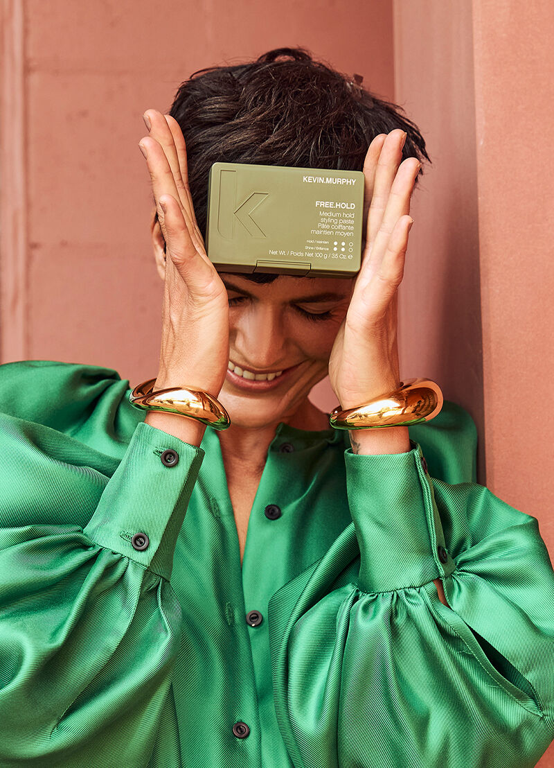 Person holding Kevin Murphy Free Hold product box in front of their face against a pink background