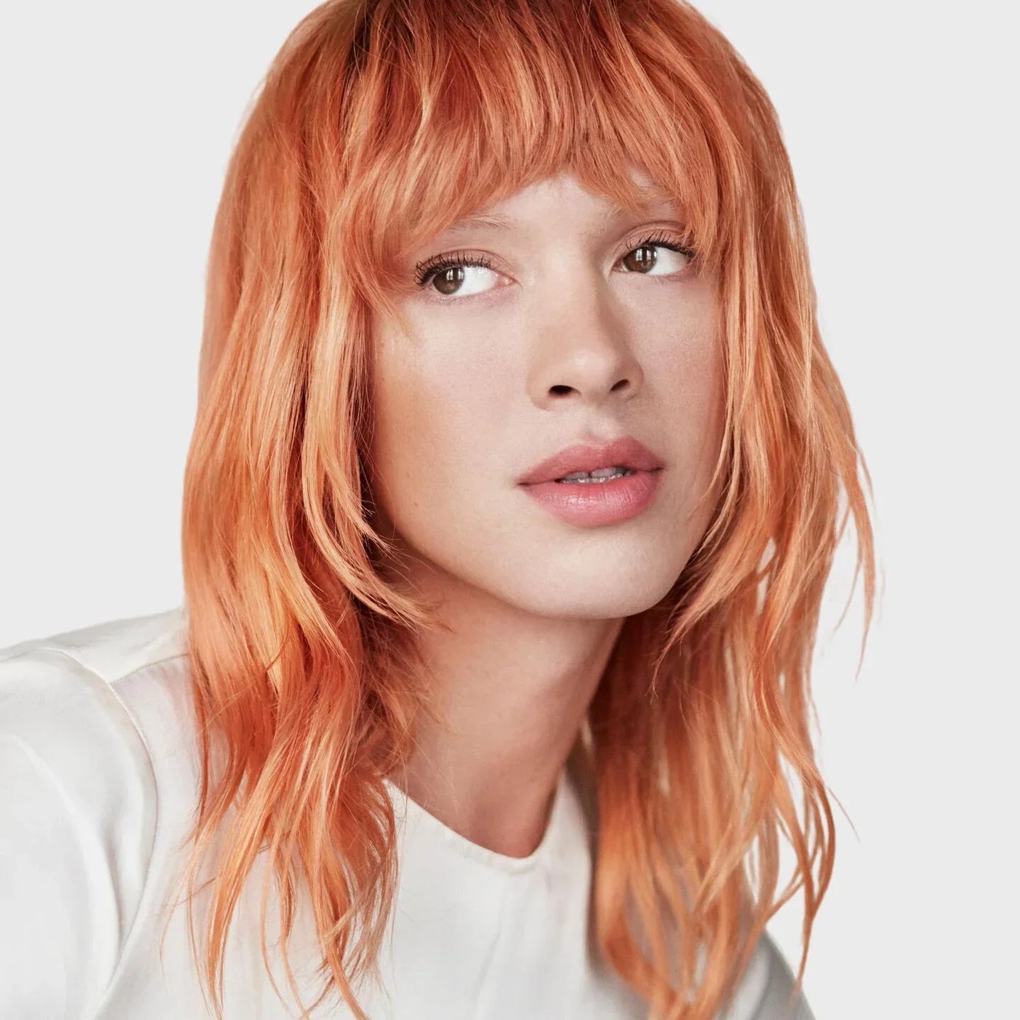 Person with copper hair wearing a white shirt on a light background