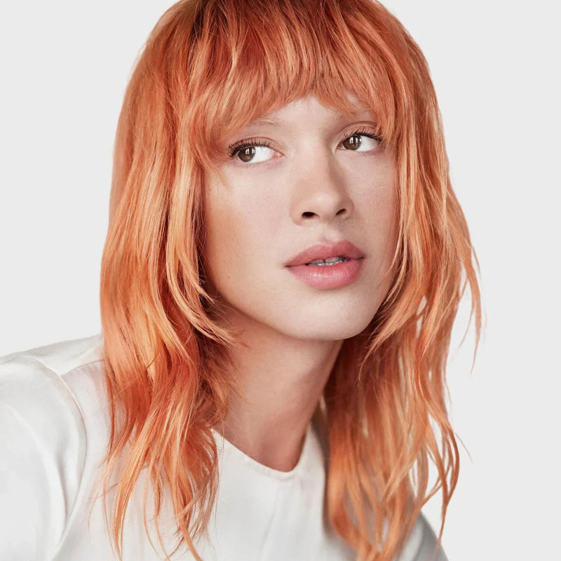 Person with copper hair wearing a white shirt on a light background