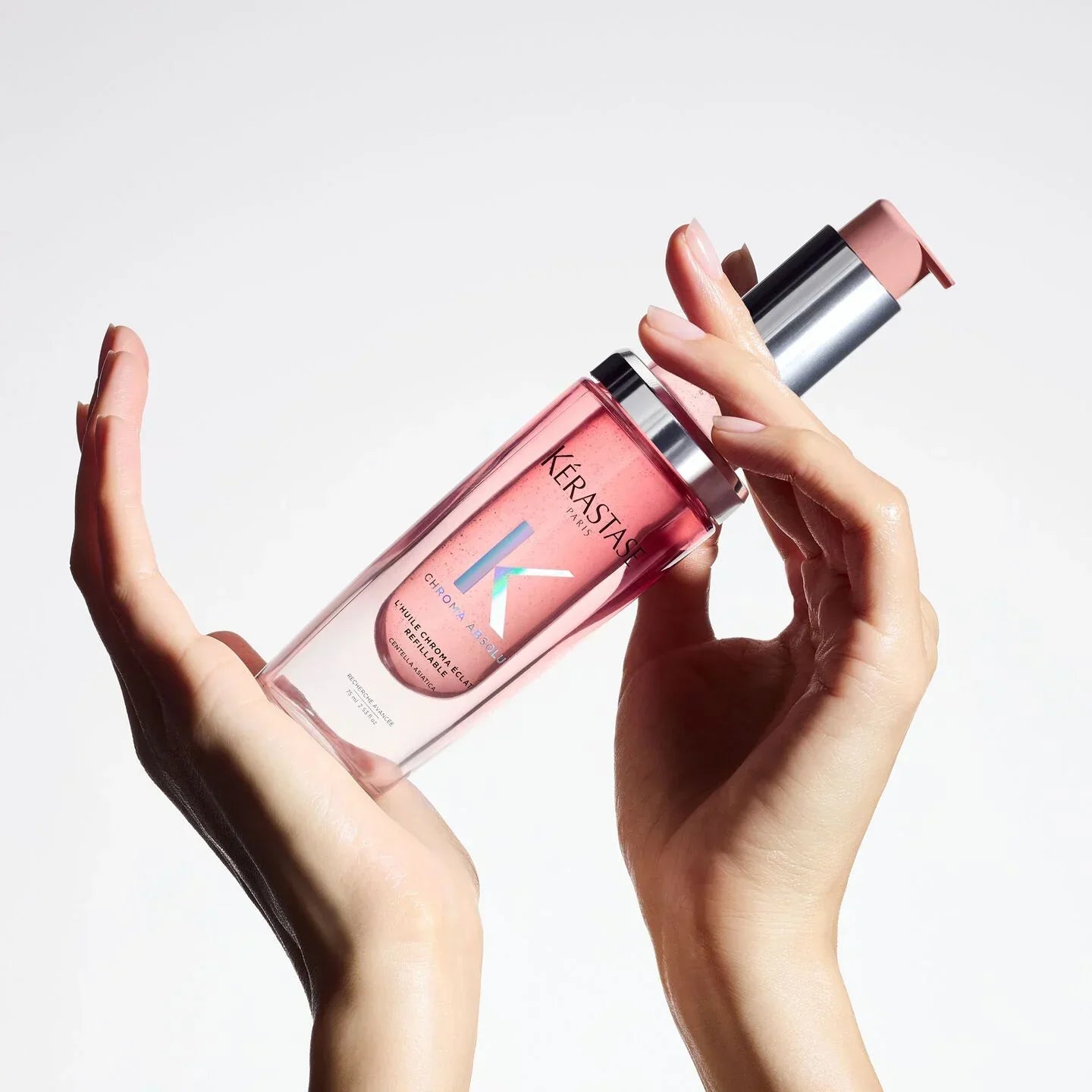 Kérastase hair product bottle held by hands against a light background