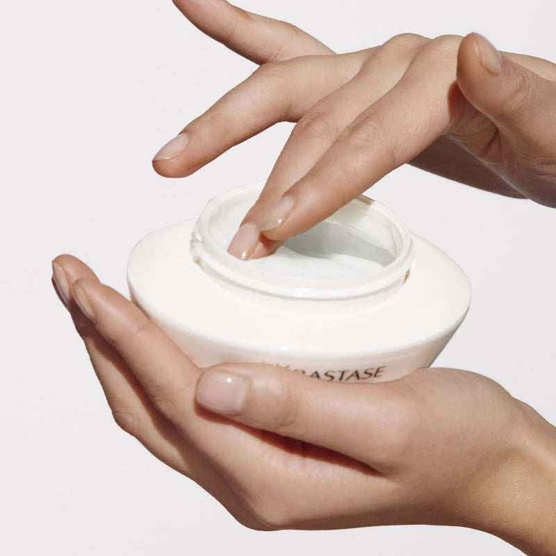 Hand holding a white jar with a brand name on a light background