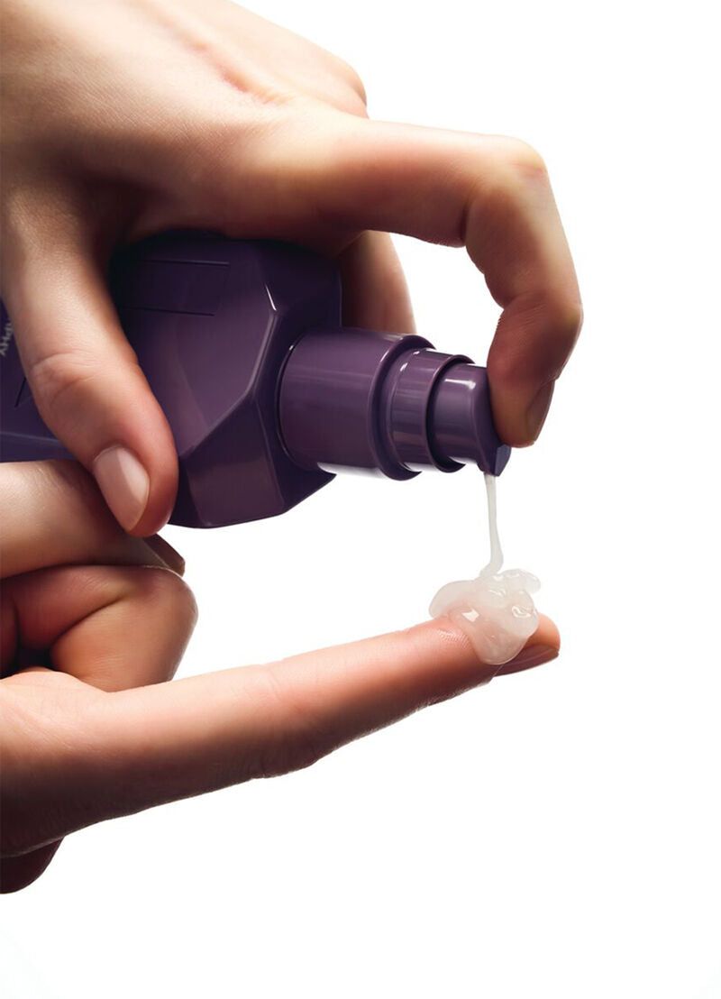 Hand holding a purple bottle with white cream being squeezed out on a white background