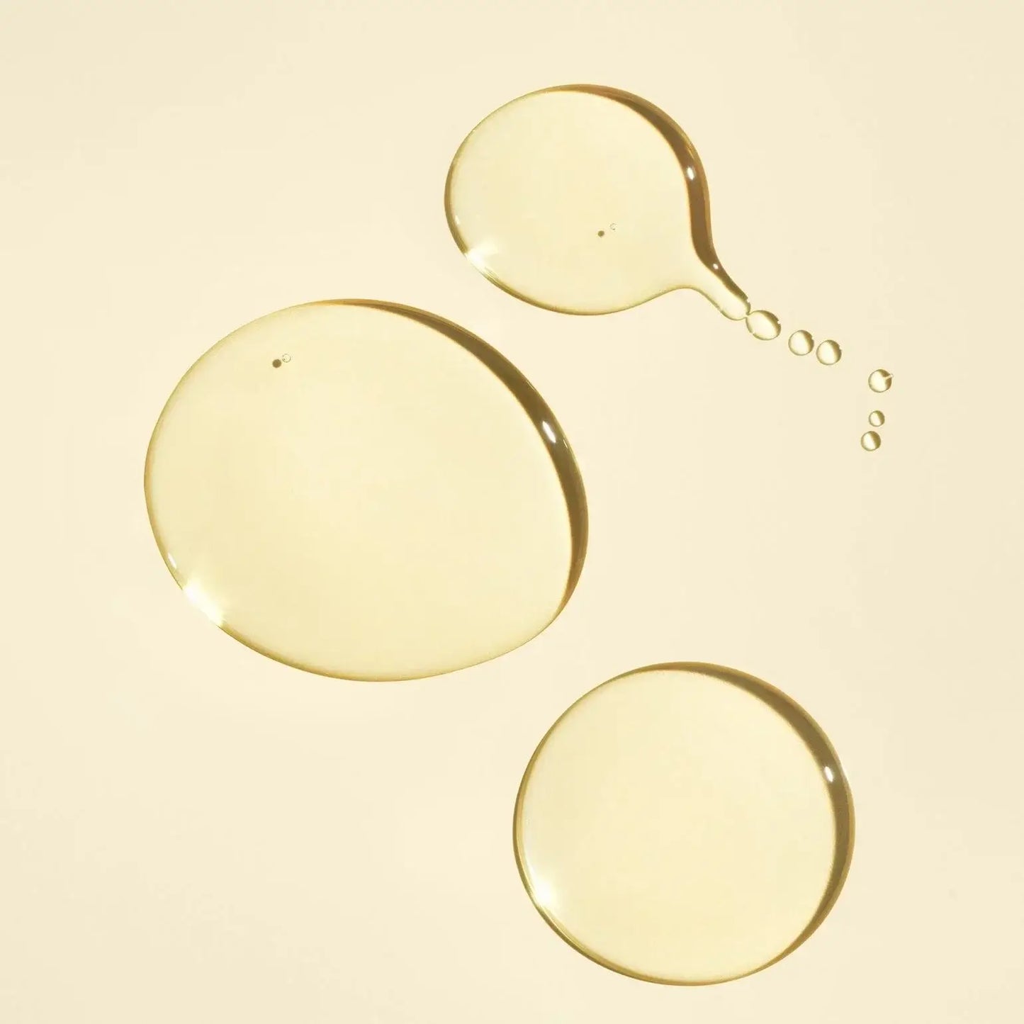 ORIBE Gold Lust Nourishing Hair Oil Texture drops on light yellow background