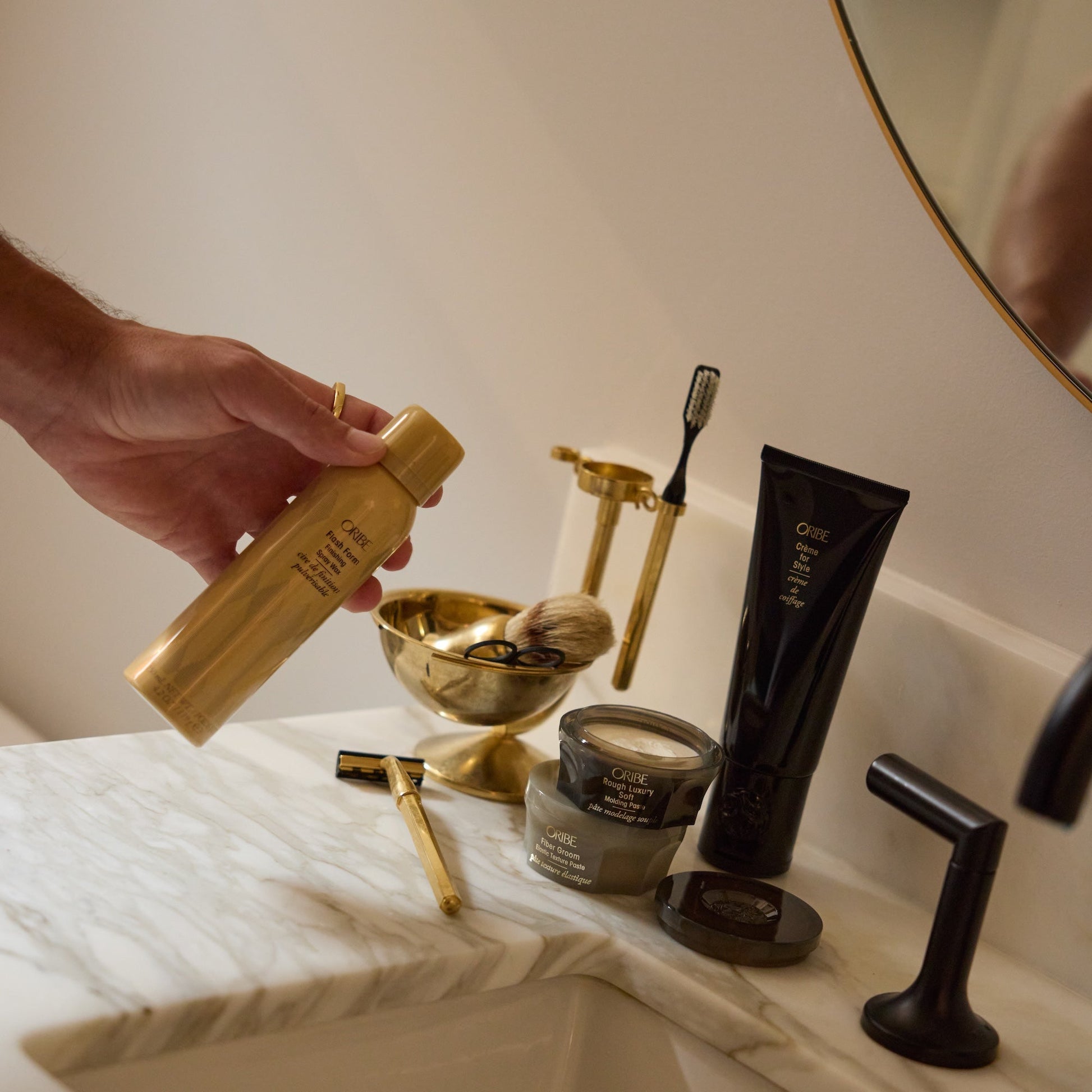 Bathroom counter with grooming products including a gold bottle, brush, and black tube.