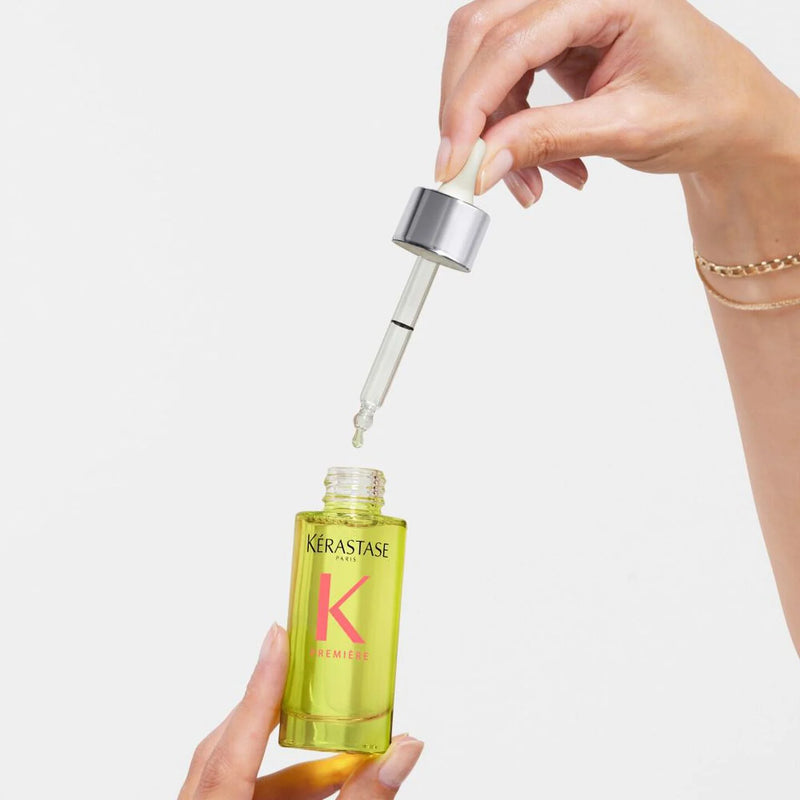 Kérastase serum bottle with dropper held by a hand on a light background