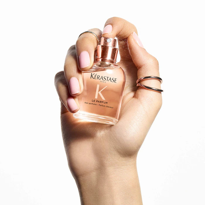 Hand holding a Kérastase perfume bottle against a white background