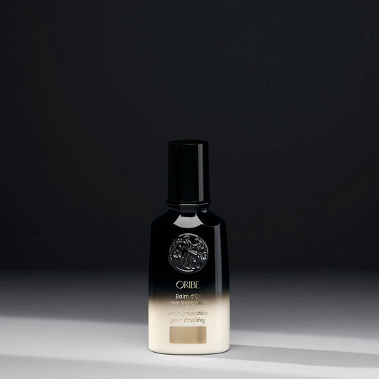 A bottle of Oribe Balm d'Or Heat Styling Shield on a dark background.