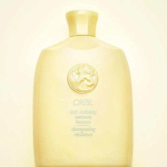 A bottle of Oribe Hair Alchemy Resilience Shampoo with a capacity of 250 ml. The bottle is beige with a gold cap and features branding and product information in white text.