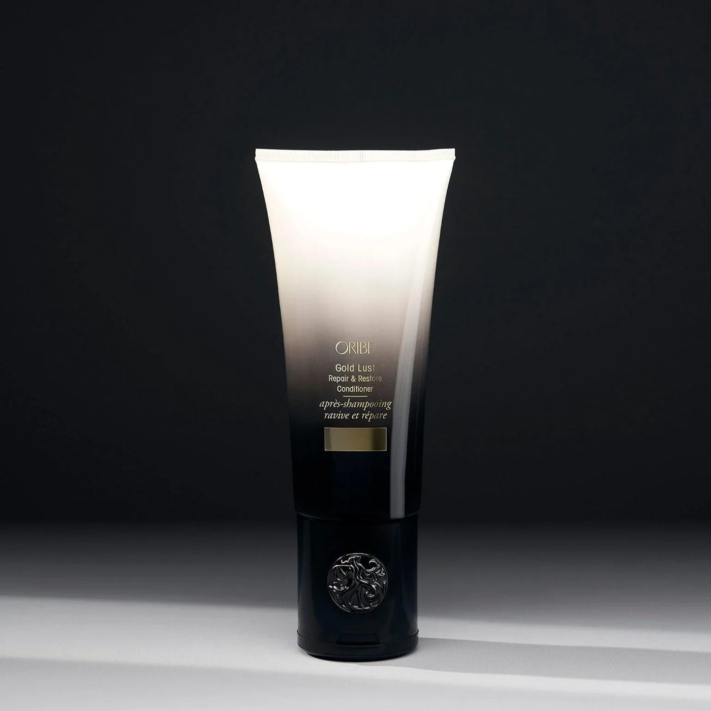 A tube of ORIBE Gold Lust Repair & Restore Conditioner against a dark background.