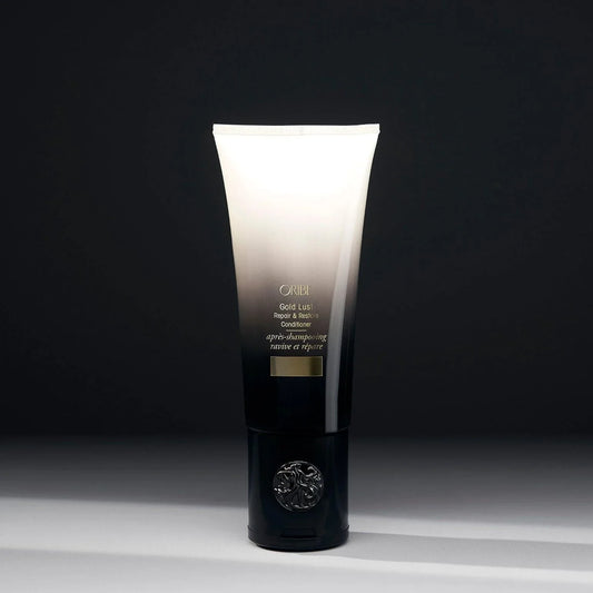 A tube of ORIBE Gold Lust Repair & Restore Conditioner against a dark background.