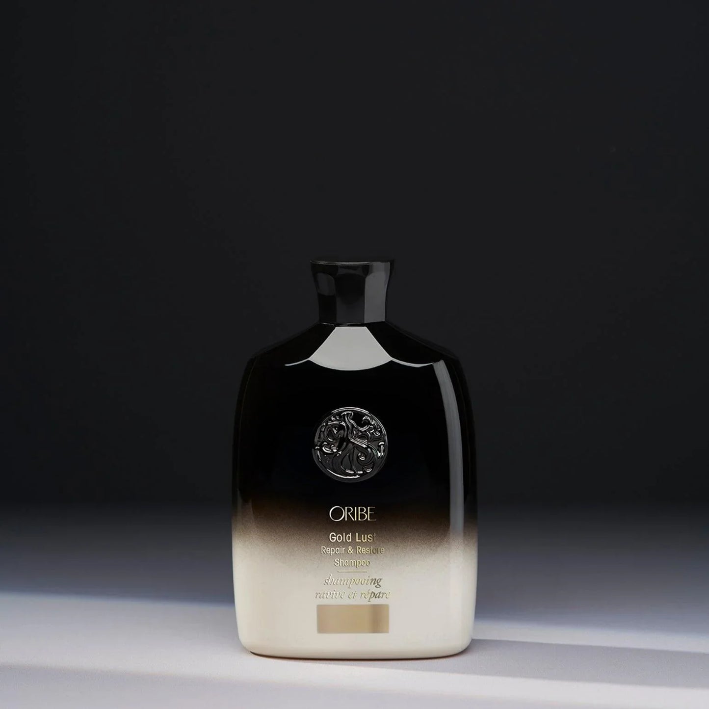 A bottle of ORIBE Gold Lust Repair & Restore Shampoo with a black to transparent gradient and gold details.