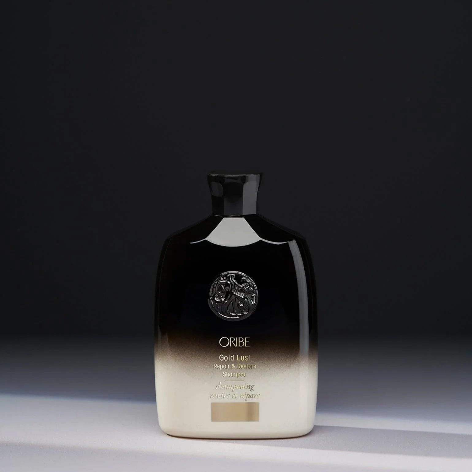 A bottle of ORIBE Gold Lust Repair & Restore Shampoo with a black to transparent gradient and gold details.