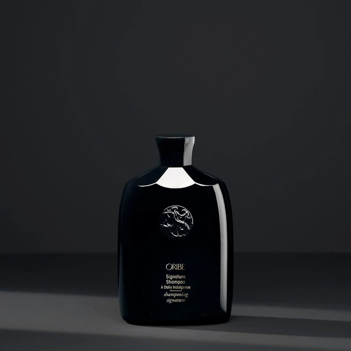 Black bottle of ORIBE Signature Shampoo with black background.