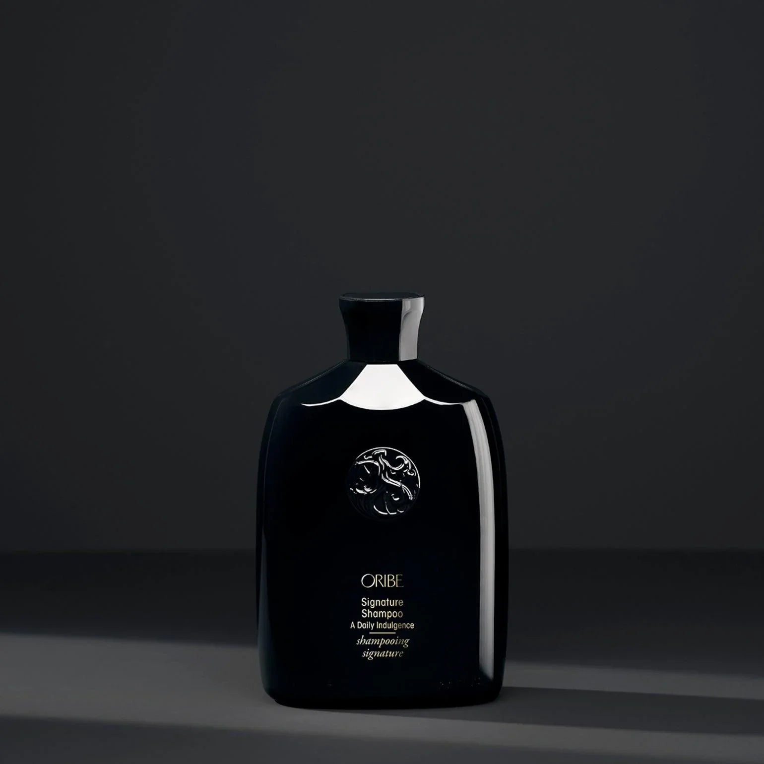 Black bottle of ORIBE Signature Shampoo with black background.