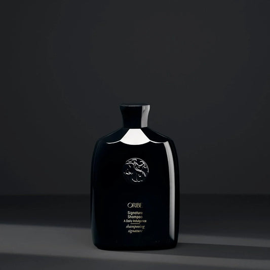 Black bottle of ORIBE Signature Shampoo with black background.