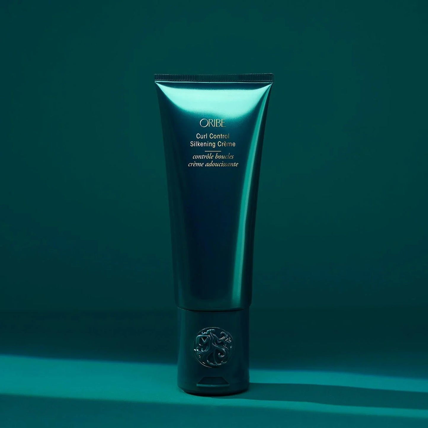 Green bottle of ORIBE Curl Control Silkening Creme with green background and light coming trhough